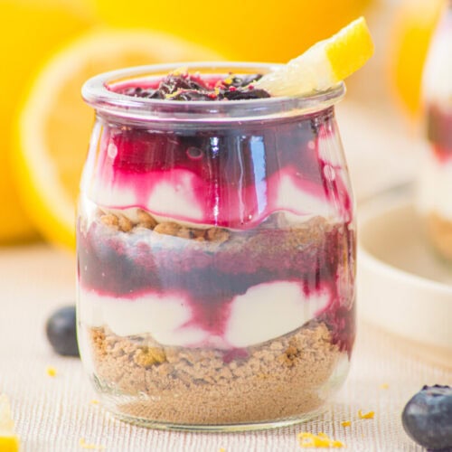 Delicious berry cheesecake parfait in a glass with layers of cream, berries, and crust.