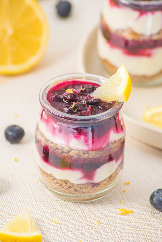 Delicious layered berry cheesecake parfait with lemon garnish in a glass jar.
