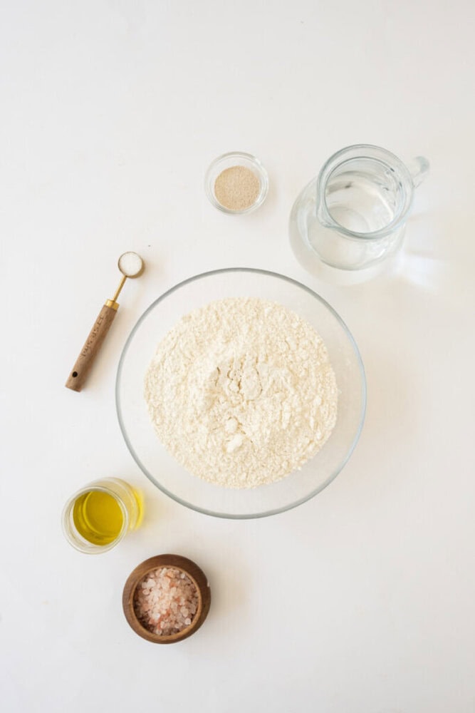 Fresh baking ingredients including flour, water, salt, yeast, olive oil, and Himalayan pink salt on.