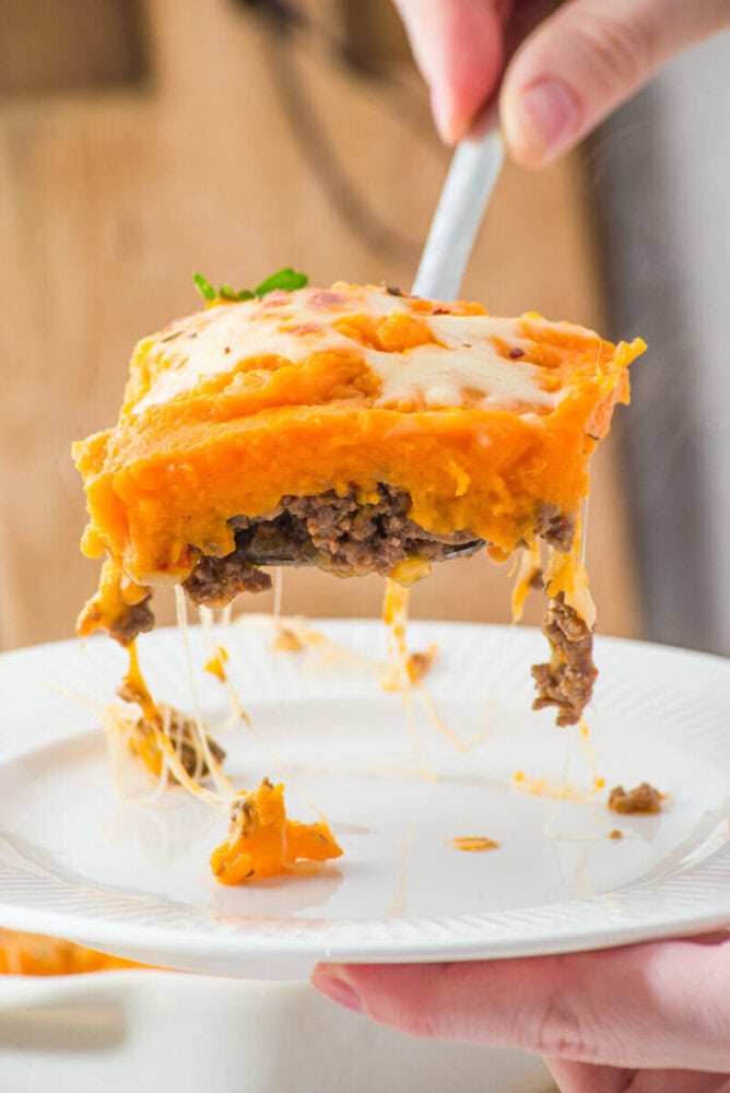 Delicious cheeseburger meatloaf topped with melted cheese and mashed potatoes, served on a white pla.