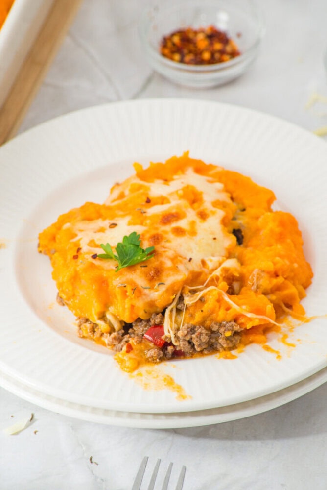Delicious cheeseburger casserole topped with melted cheese and mashed potatoes, served on a white pl.