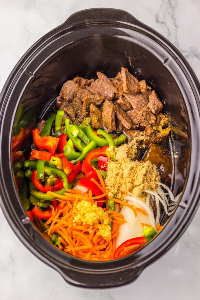 Slow cooker beef with colorful vegetables and seasonings in a black crockpot.