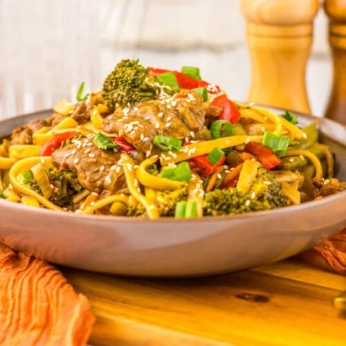 Delicious beef and vegetable stir-fry with broccoli, peppers, and noodles on a rustic wooden table.