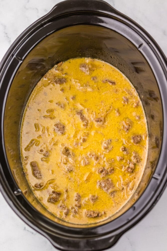 Creamy beef stew cooking in a slow cooker with tender beef and vegetables.