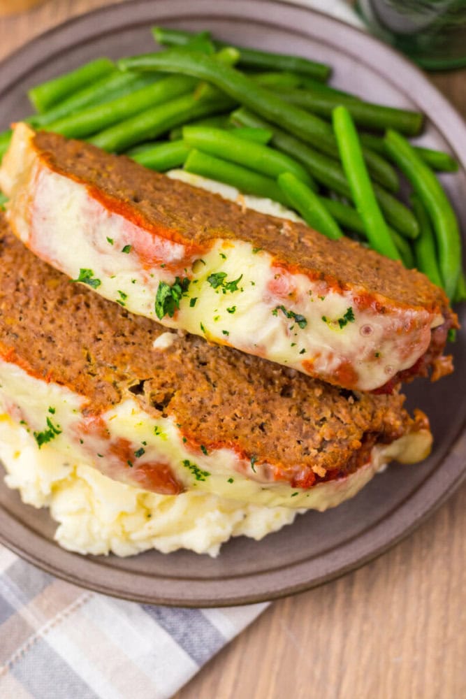 Delicious homemade meatloaf served with mashed potatoes and green beans on a plate.