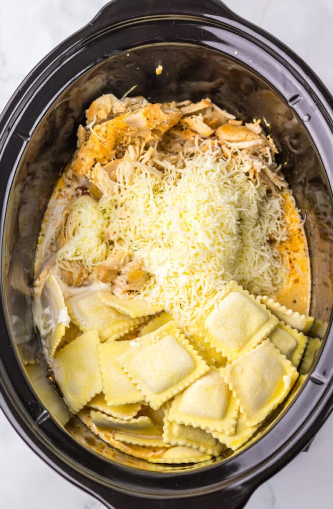 Creamy chicken and cheese ravioli cooking in a slow cooker with cheese and herbs.