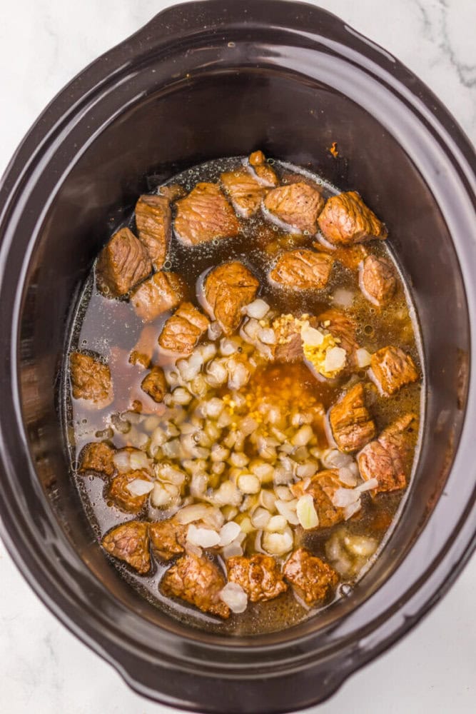 Slow cooker beef stew with tender beef chunks, onions, and garlic in savory broth.