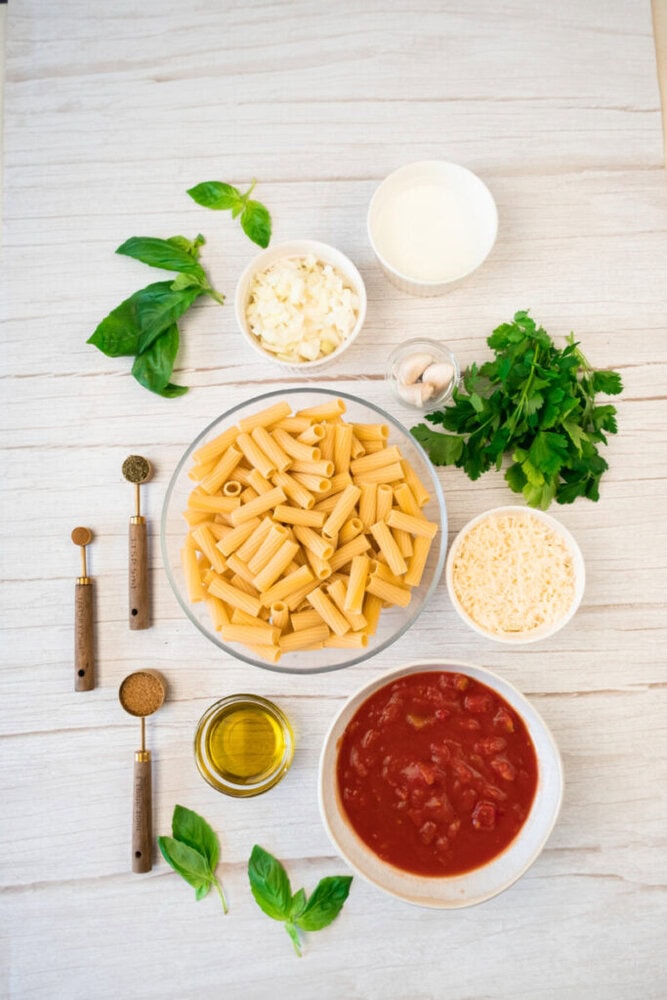 Cooked pasta with fresh tomato sauce, basil, and cheese on a white wooden surface.