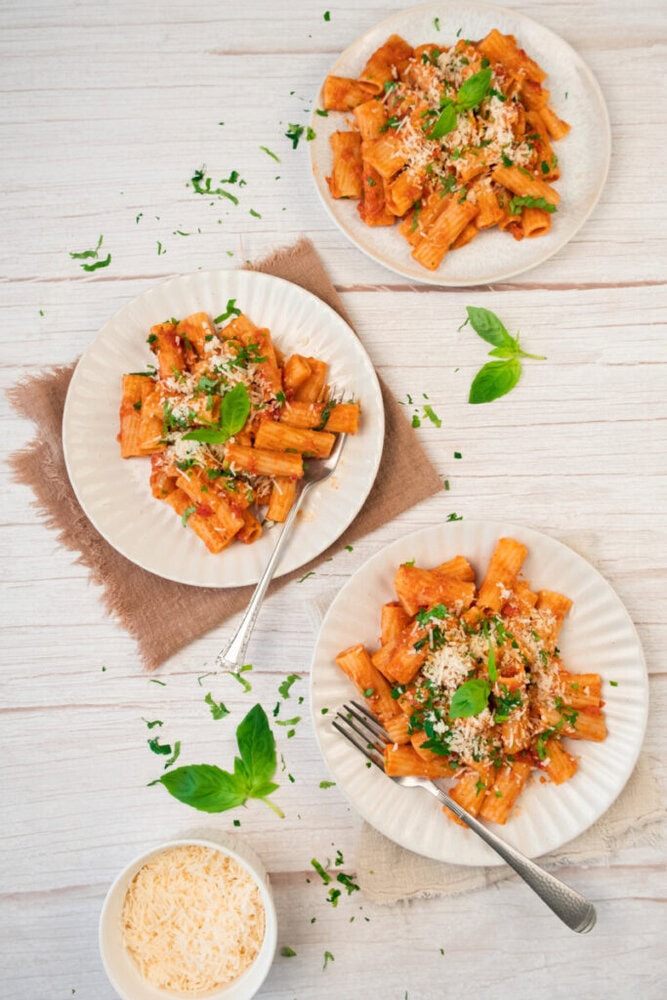 Creamy tomato pasta with fresh basil and grated cheese on white plates.