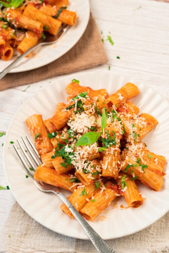 Creamy tomato pasta with grated Parmesan cheese and fresh basil leaves on a white plate.