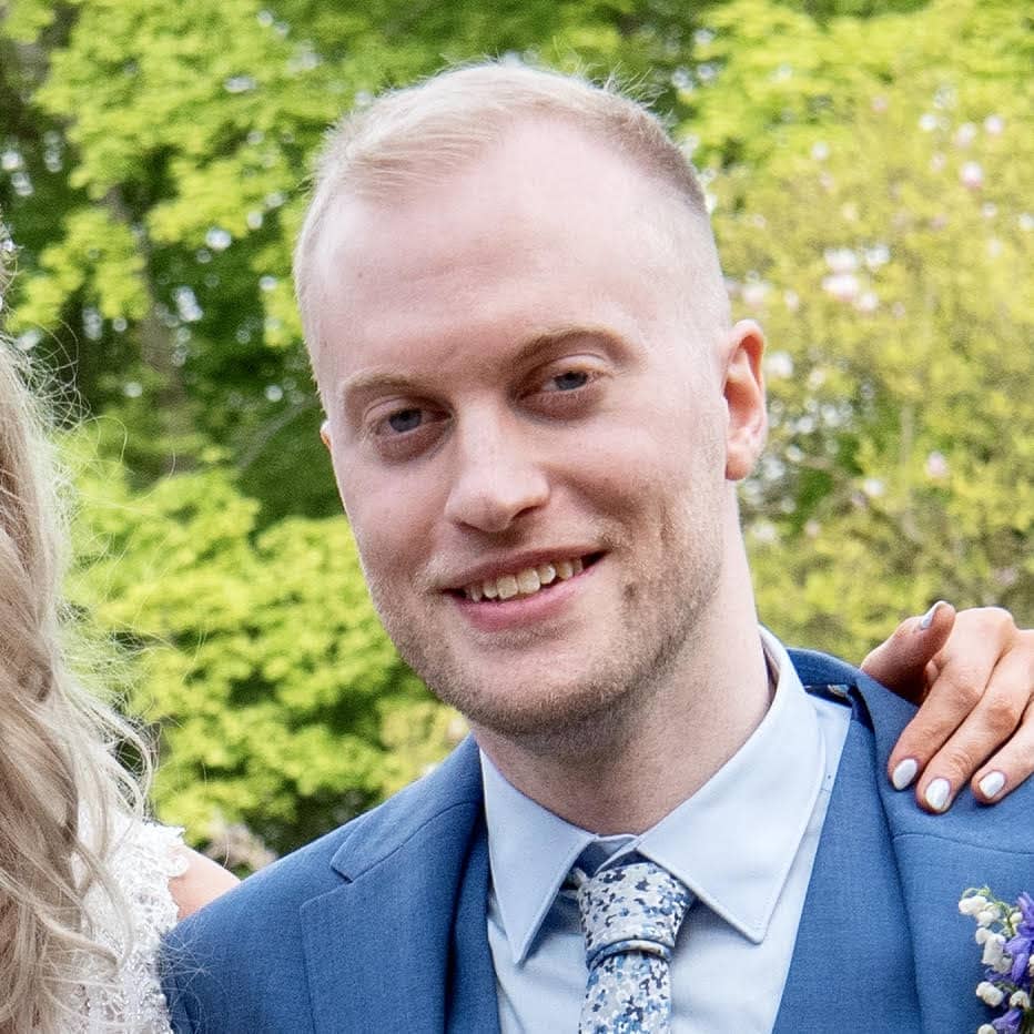 Smiling man in a blue suit at an outdoor wedding event.