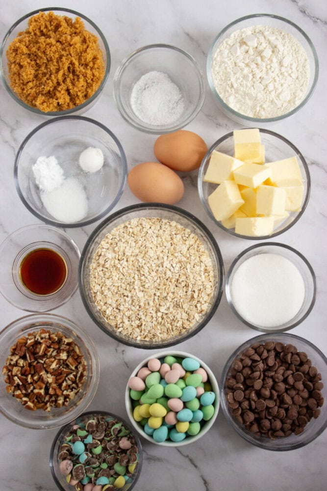 Baking ingredients including oats, butter, eggs, sugar, and chocolate chips arranged on a marble sur.