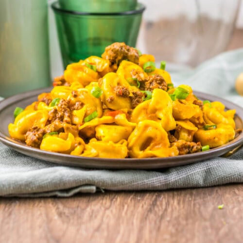 Delicious cheesy beef tortellini served on a dark plate with a rustic background.
