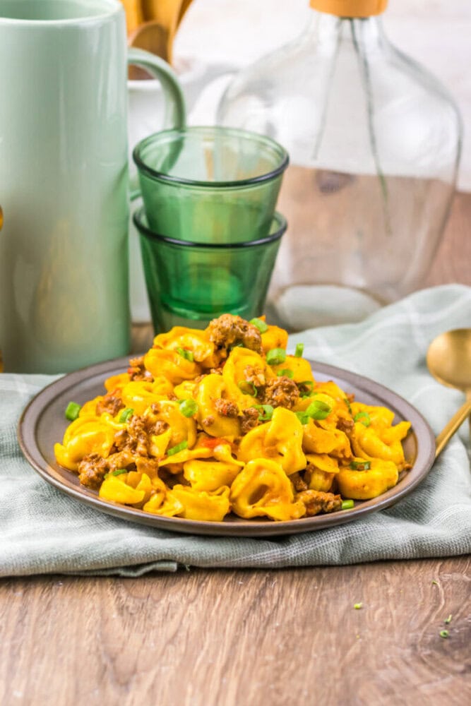 Delicious beef and tortellini pasta with creamy sauce and green peas on a rustic wooden table.