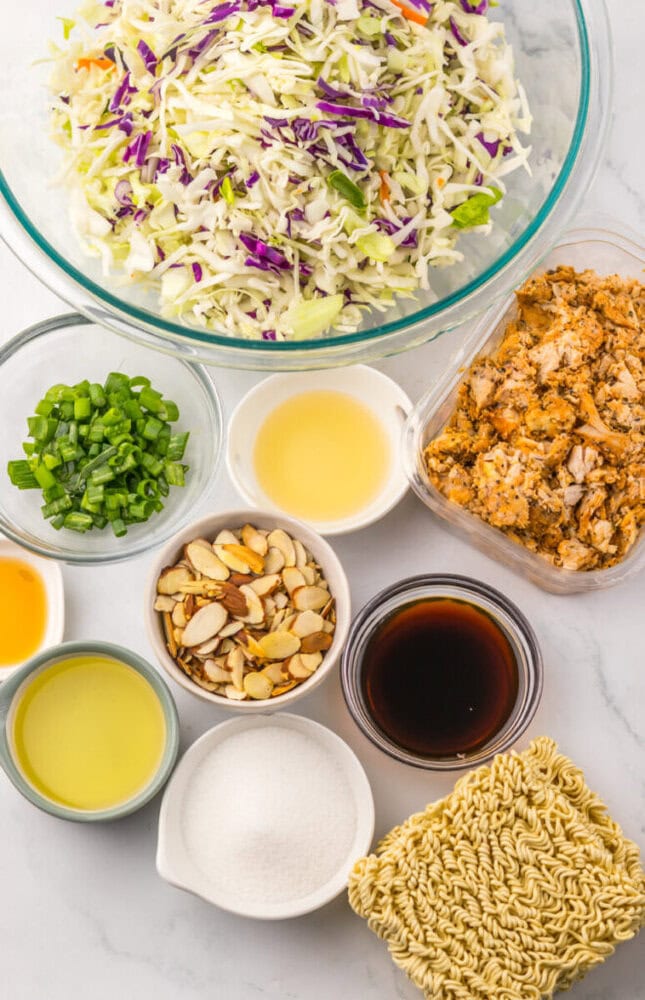 Ingredients for cabbage slaw with nuts and dressing in bowls and a large glass mixing bowl.