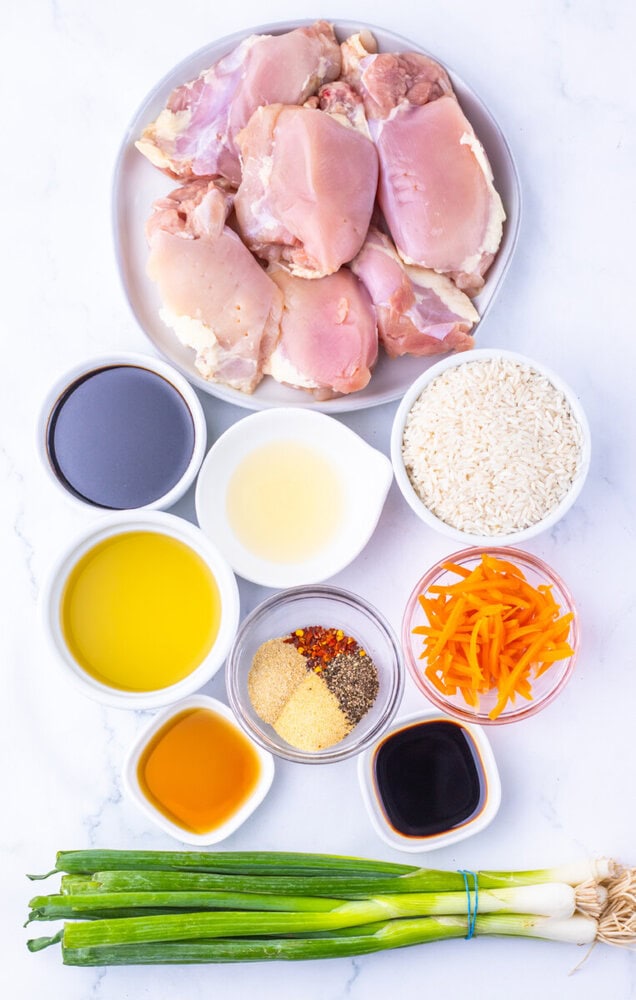Fresh chicken thighs on a white plate with various seasonings and ingredients.