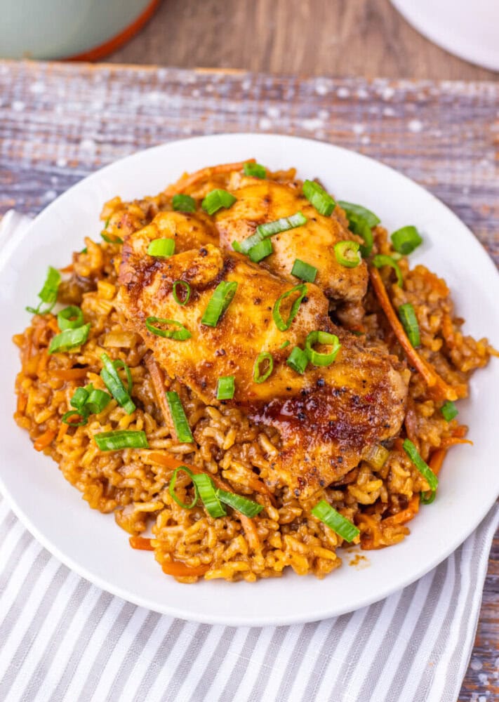 Baked chicken thigh with seasoned rice and green onions on a white plate.