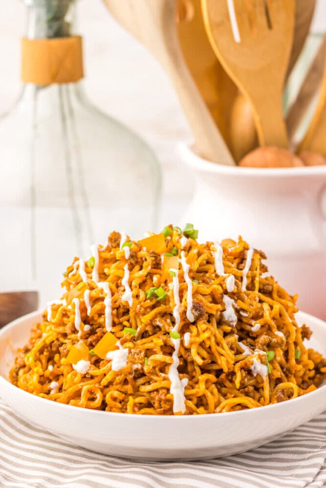Delicious spicy chicken ramen noodles garnished with green onions and drizzled with white sauce.