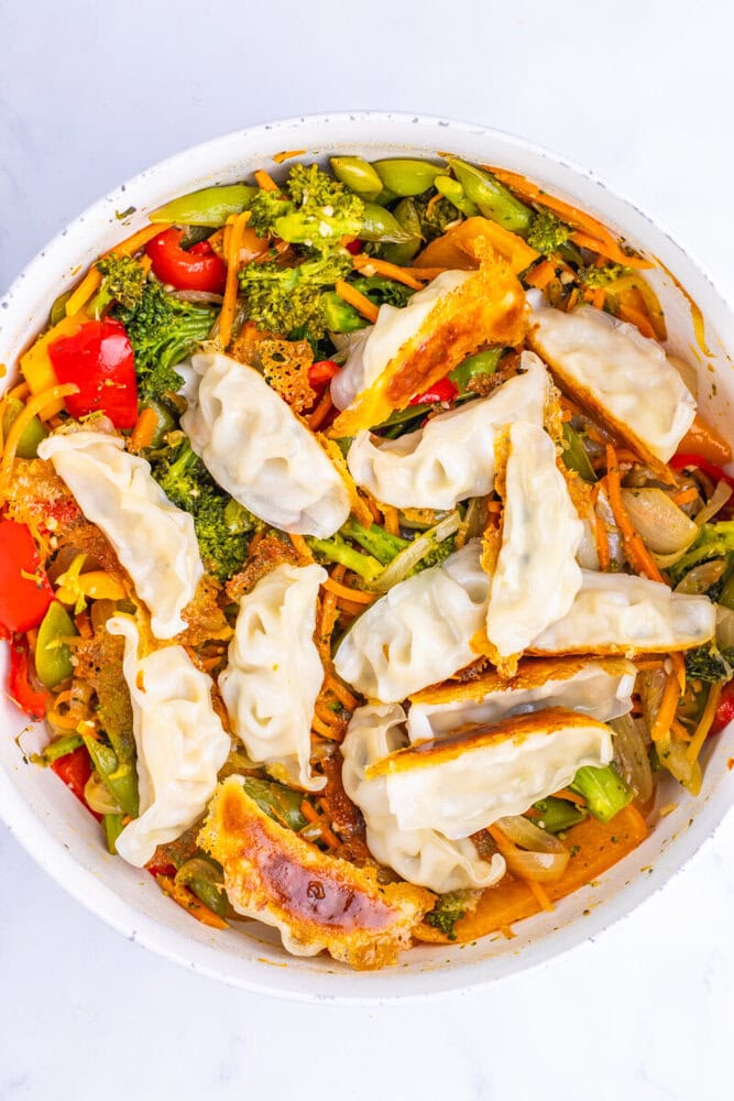 Vegetable dumplings with stir-fried broccoli, bell peppers, carrots, and green beans in a white bowl.