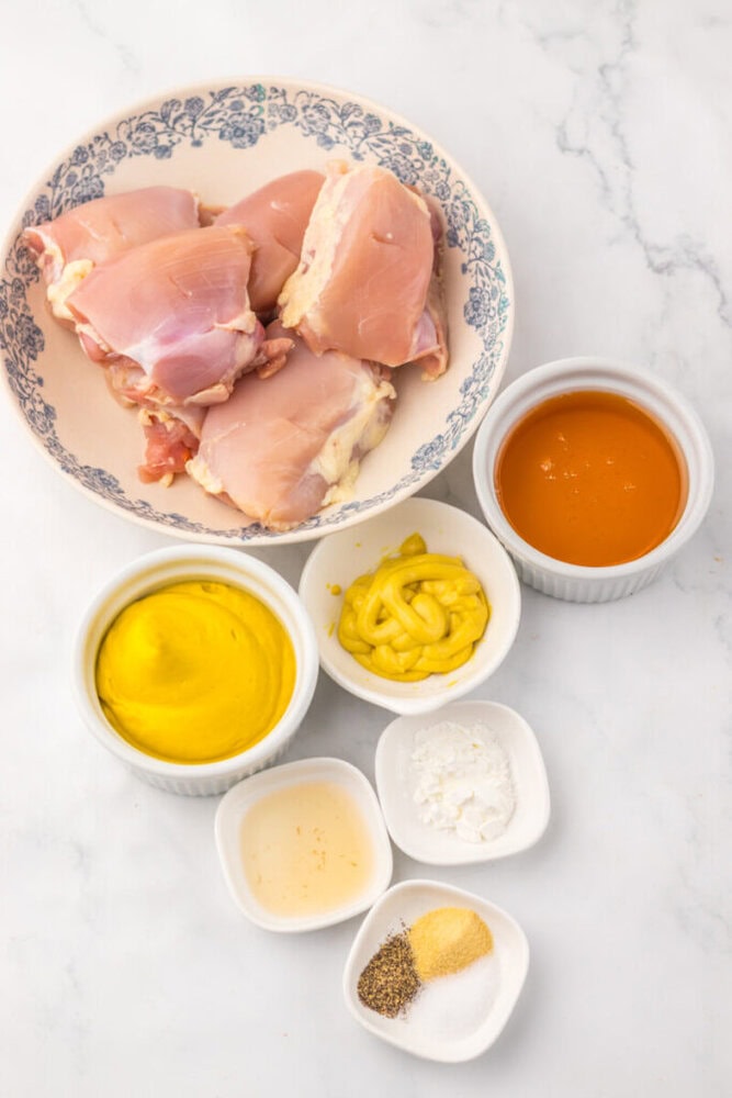 Raw chicken thighs with honey mustard sauce and spices on a white marble surface.