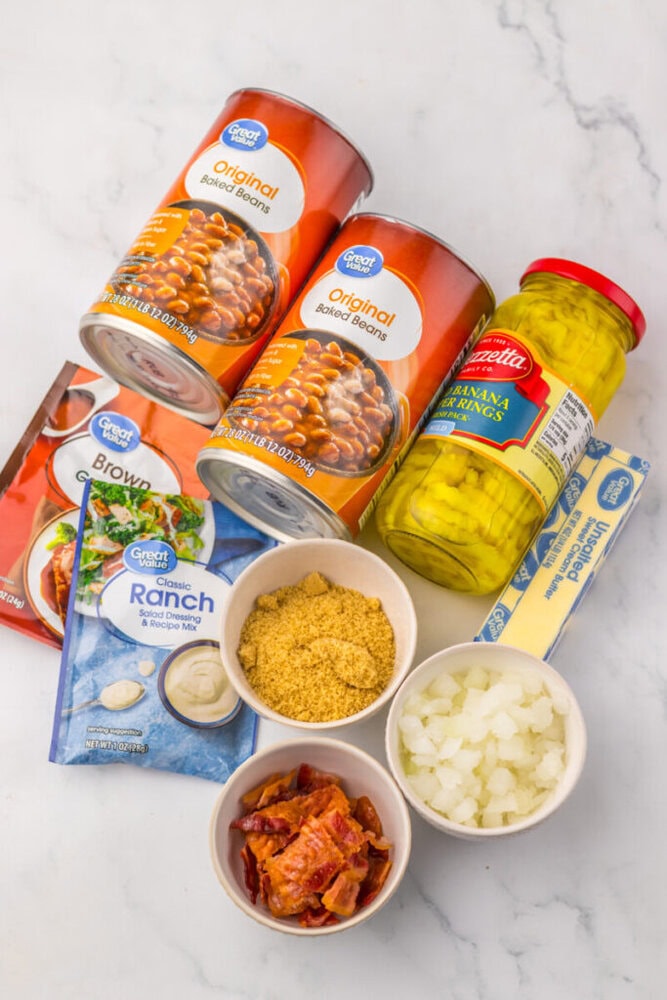 Canned baked beans, pickles, sour cream, and chopped onions arranged on a white surface.