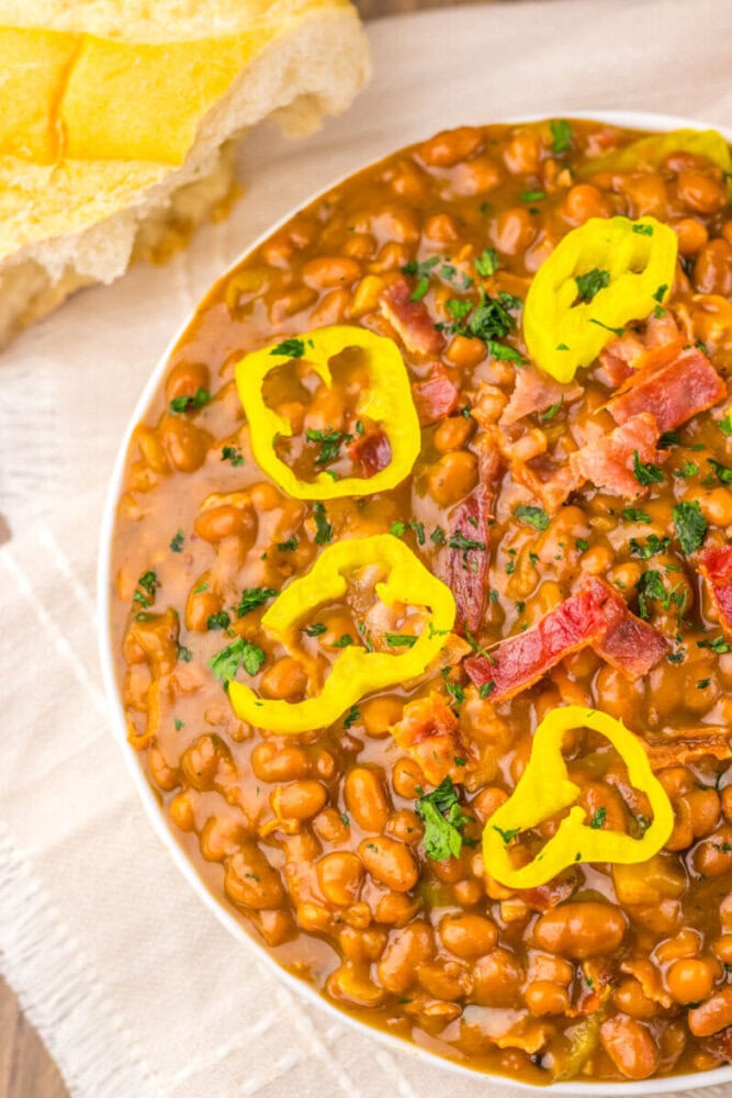 Delicious bean chili with bacon, peppers, and herbs in a white bowl.