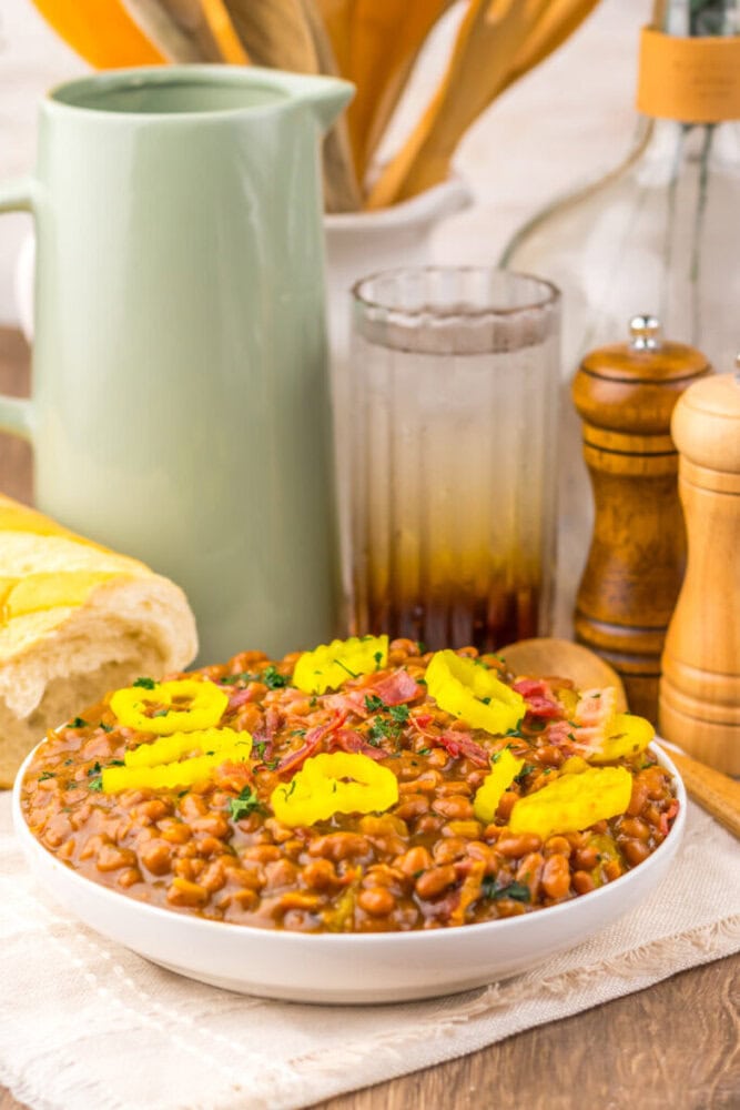Hearty bean chili topped with sliced pickled jalapeños, served in a white bowl on a rustic kitchen t.