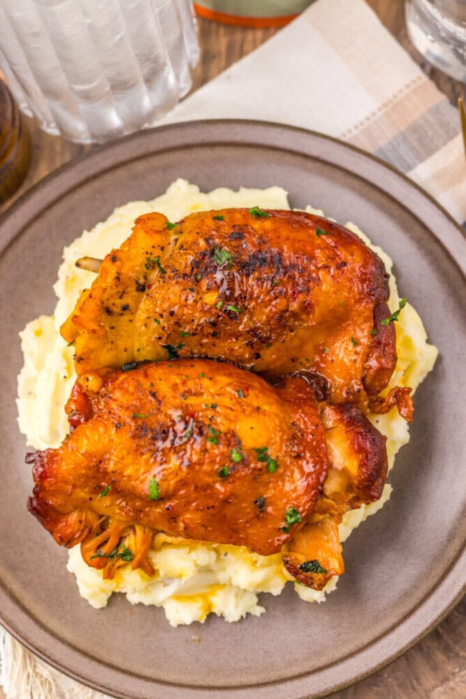 Delicious roasted chicken thighs served over creamy mashed potatoes, garnished with herbs for a hear.