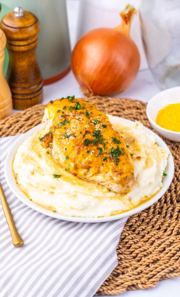 Juicy baked chicken breast served over creamy mashed potatoes, garnished with herbs.