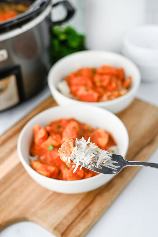 Delicious creamy tomato chicken stew served in white bowls with rice, on a wooden board.