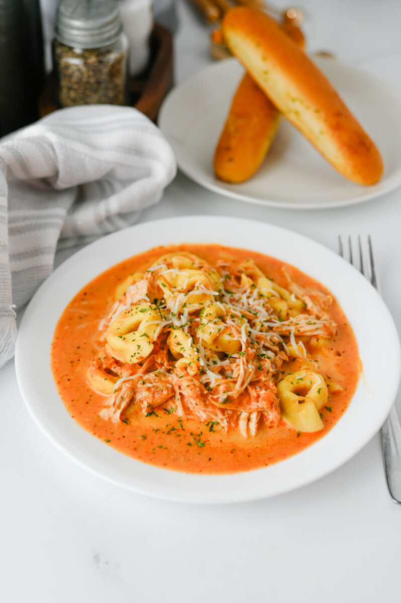 Crock Pot Chicken Tortellini with shrimp in creamy tomato sauce, garnished with parsley, plated on white dish