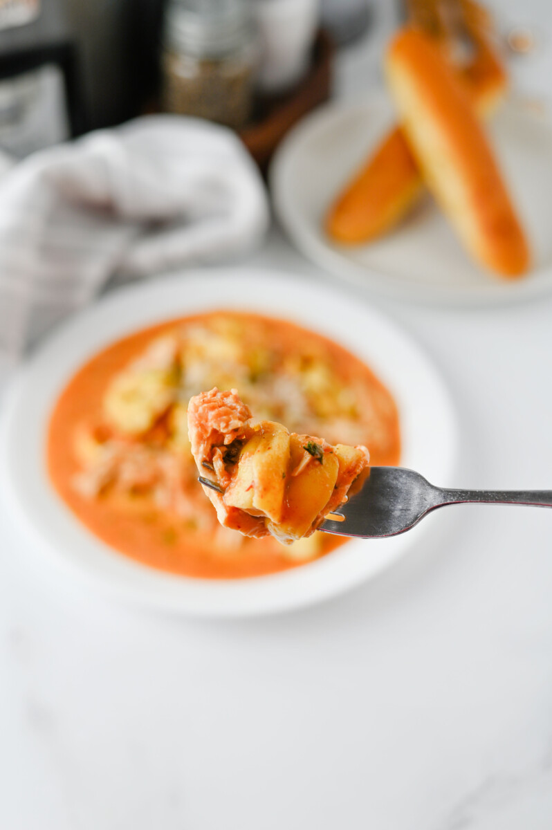 Close-up of a forkful of chicken tortellini in creamy tomato soup from slow cooker recipe