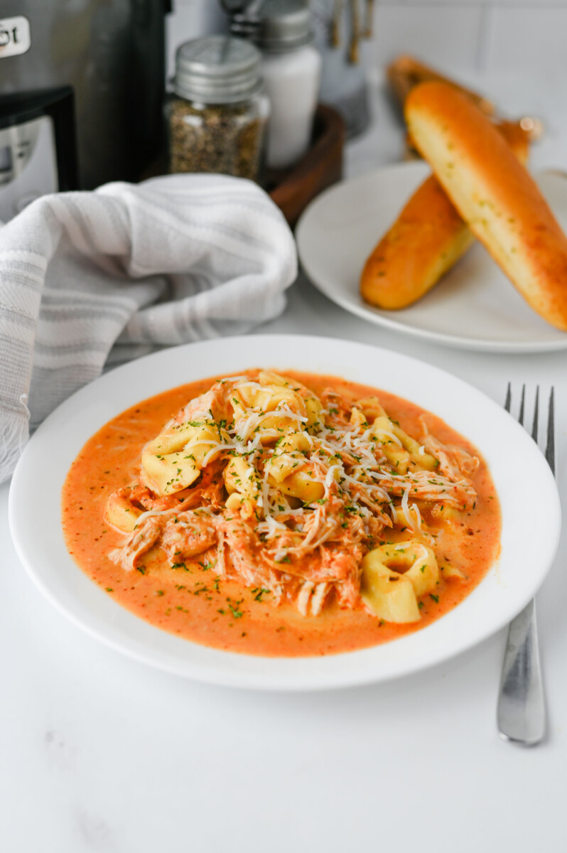 Crock pot chicken tortellini in creamy tomato sauce garnished with parmesan cheese and fresh herbs, plated and ready to serve