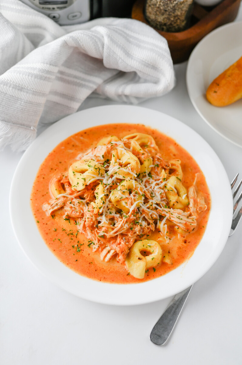 Crock Pot Chicken Tortellini in creamy red sauce topped with shredded chicken and parmesan cheese
