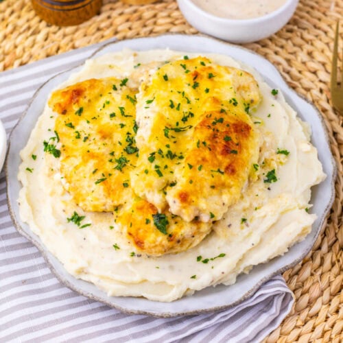 Juicy baked chicken breast served over creamy mashed potatoes, garnished with herbs.