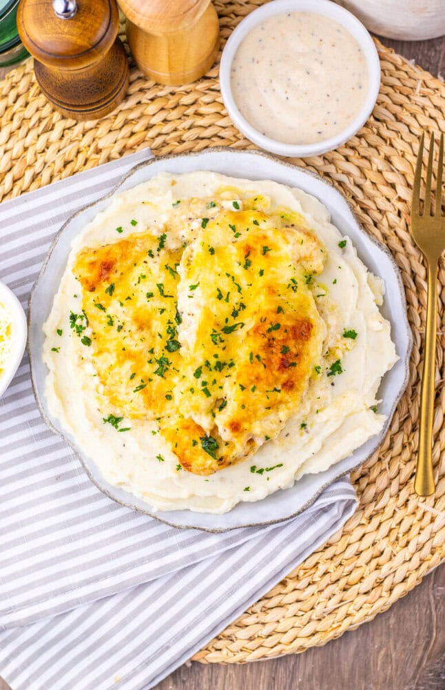 Creamy chicken caesar bake with melted cheese and parsley garnish on white plate with mashed potatoes