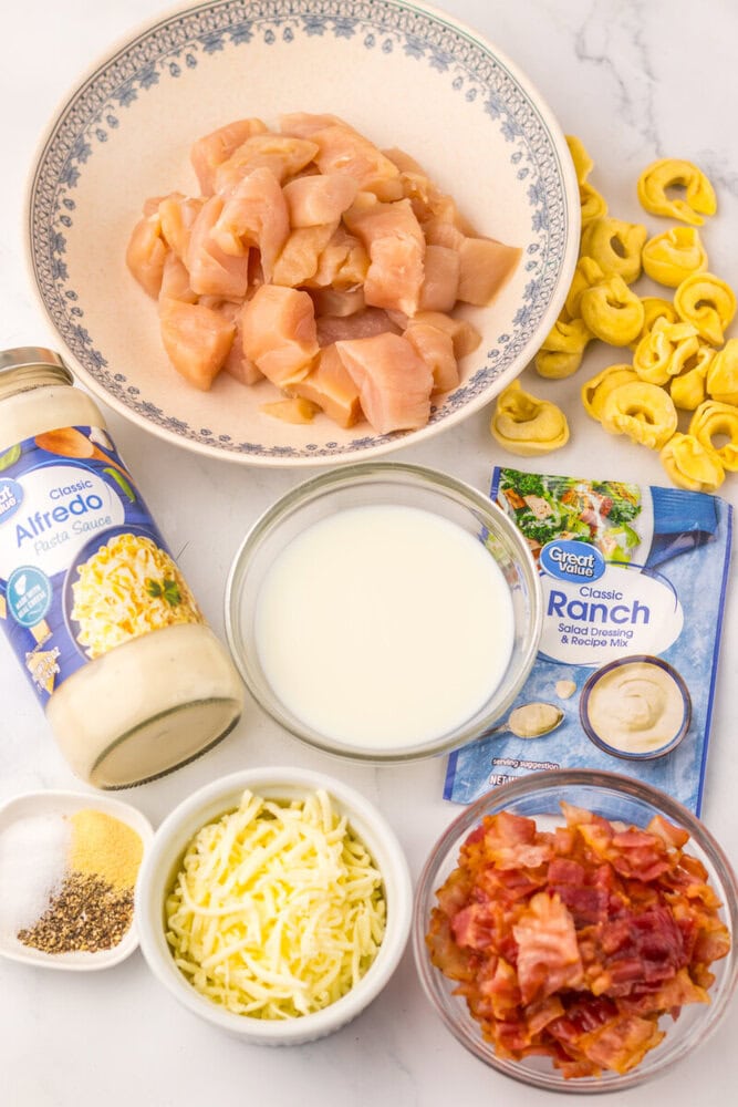Sheet Pan Chicken Bacon Ranch Tortellini ingredients laid out including raw chicken, tortellini pasta, bacon, cheese, ranch seasoning, and sauce components