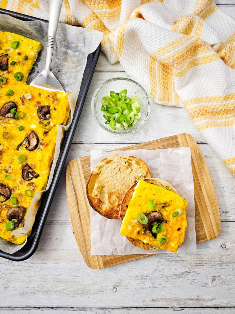 Delicious mushroom and cheese frittata slice with green onions on a wooden board.