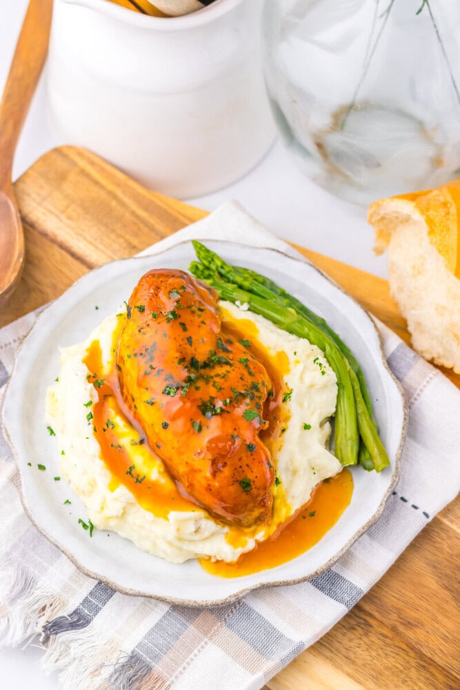Slow cooker apricot brown sugar chicken plated with mashed potatoes and asparagus, garnished with fresh herbs