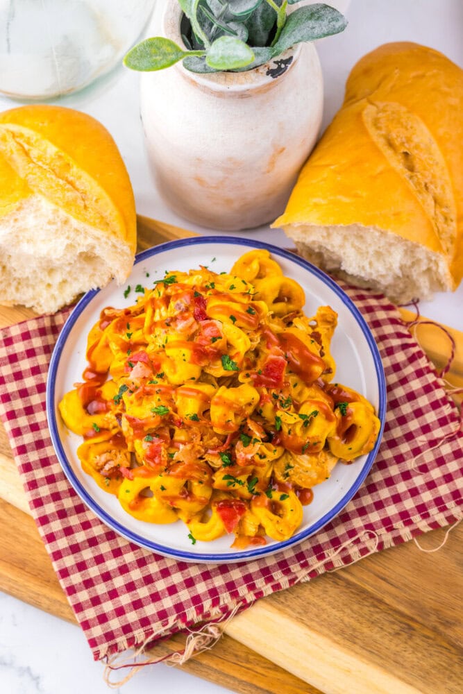 Slow cooker cheesy BBQ bacon chicken tortellini plated and ready to serve with bread and fresh garnish