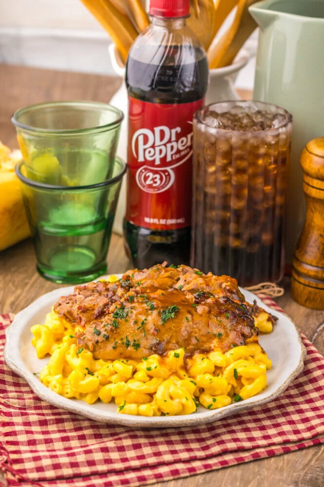 Slow cooker Dr Pepper BBQ brisket with mac and cheese plated on white dish with Dr Pepper bottle and beverages in background