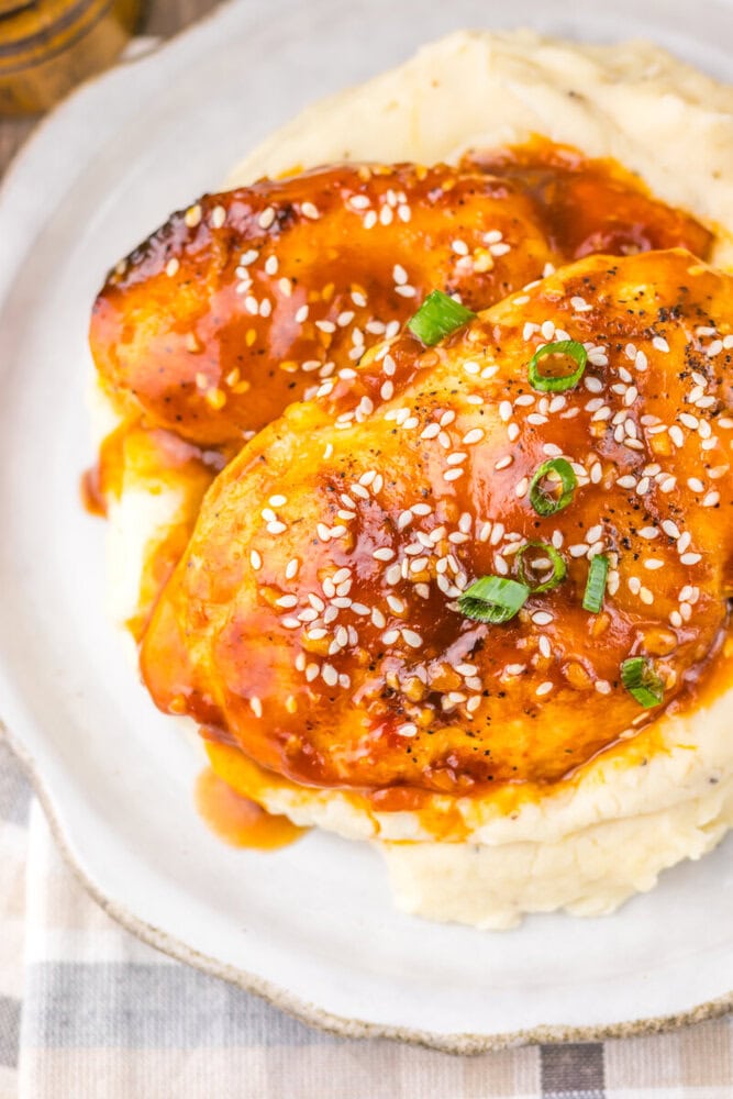Slow cooker honey sesame chicken sandwich with sesame seeds and green onions on white plate