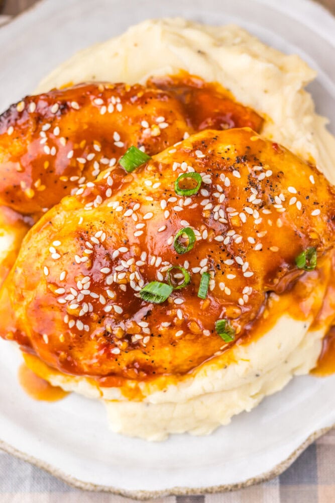 Delicious baked chicken topped with savory sauce, sesame seeds, and green onions served over creamy.