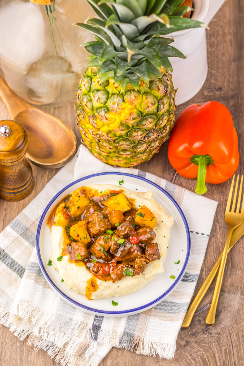 Fresh pineapple and red bell pepper with a plate of savory stew on a rustic wooden table.