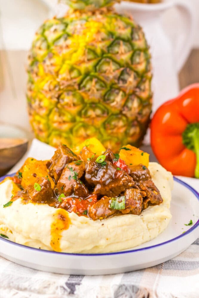 Beef stew served on a bed of mashed potatoes with fresh pineapple and colorful vegetables.