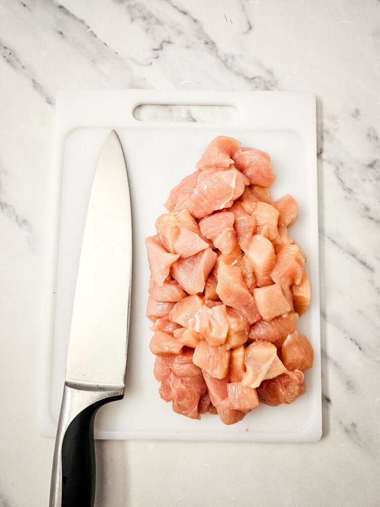 Fresh chicken breast cubes on a white cutting board with a knife.