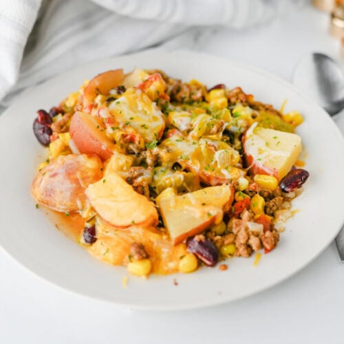 Delicious chicken and rice casserole with vegetables and cheese on a white plate.