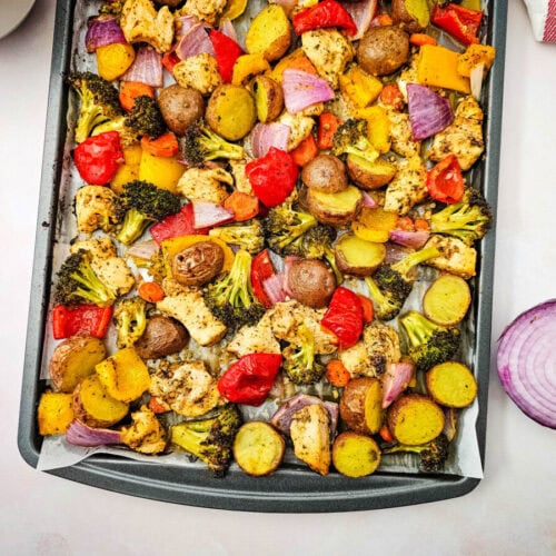 Colorful roasted vegetables including broccoli, potatoes, red peppers, and onions on baking sheet.