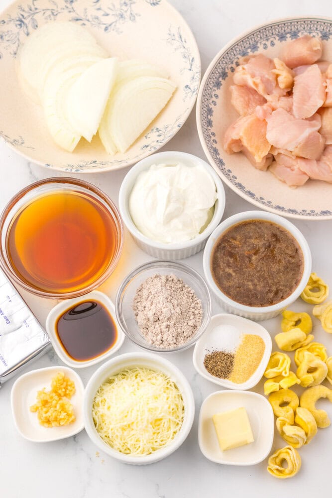 Assorted ingredients for creamy chicken pasta including chicken, onions, cheese, and seasonings.