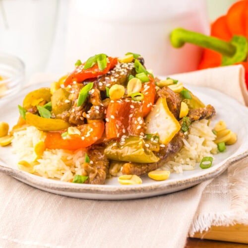 Colorful stir-fried vegetable and beef served over rice on a white plate.